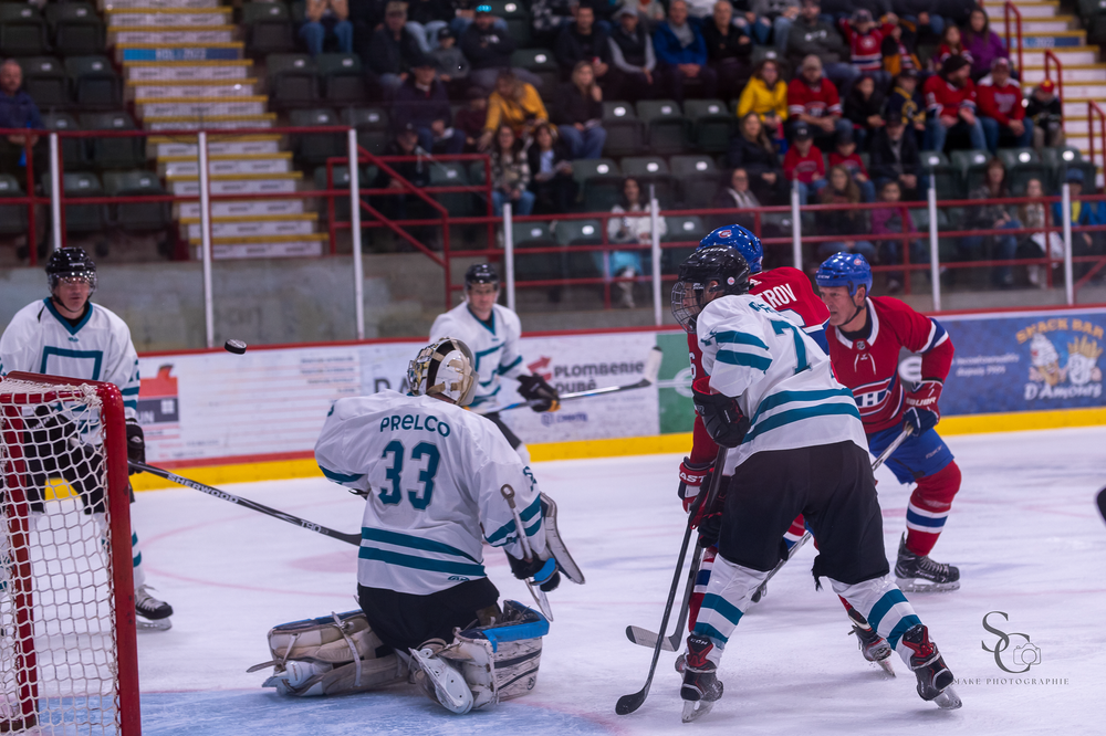 Hockey players compete near the goal with goalie in position during intense gameplay.