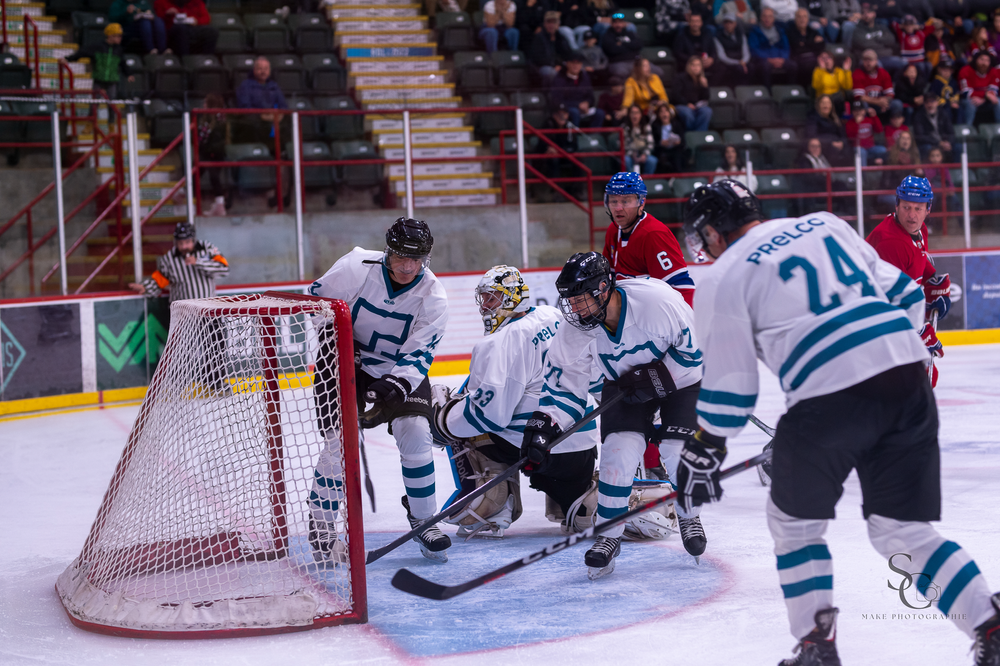 Hockey players crowd around the net during a tense defensive play.