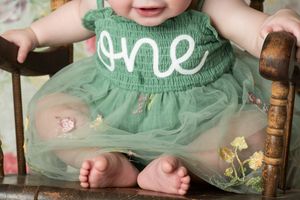 Close-up view of a mint green tulle dress with 'one' text detail on a wooden vintage chair.