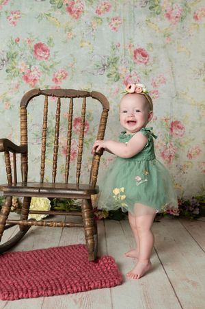 Vintage wooden rocking chair against floral wallpaper with pink rug on light wooden floor.