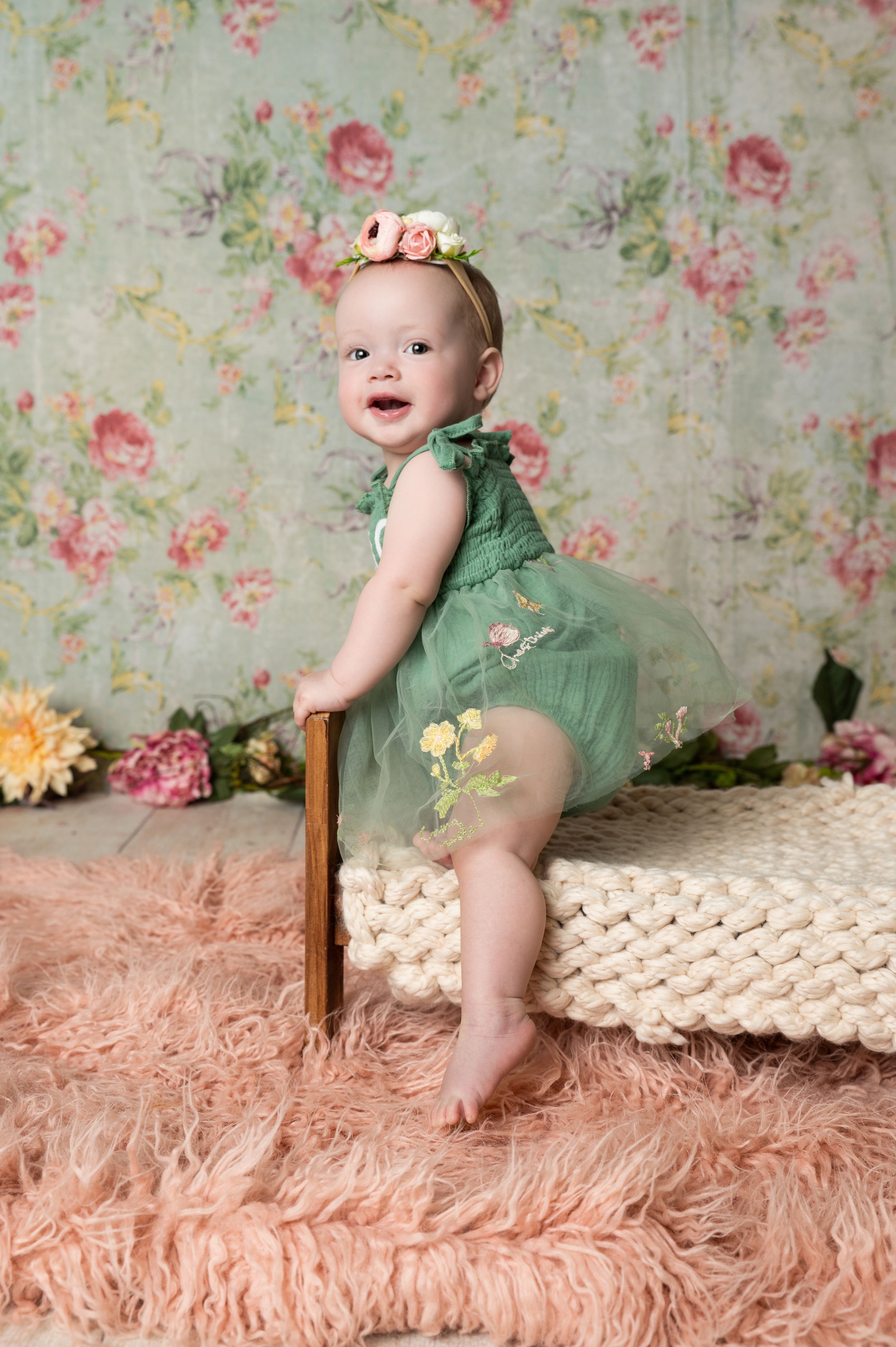 Sweet portrait of a baby wearing a mint green tulle dress and floral crown against a vintage floral backdrop.