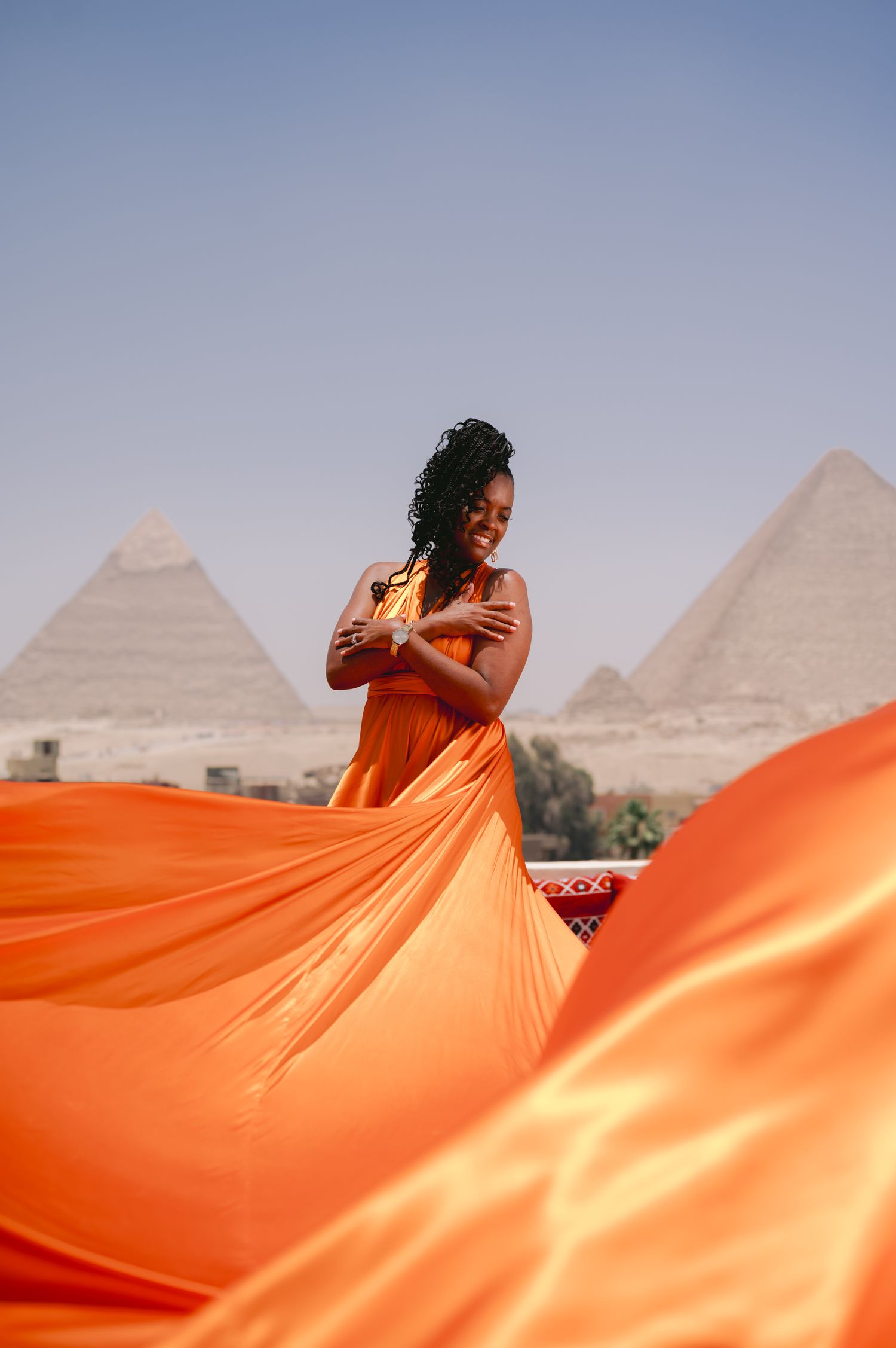 A flowing orange dress billows dramatically against the backdrop of the ancient Egyptian pyramids in Giza.