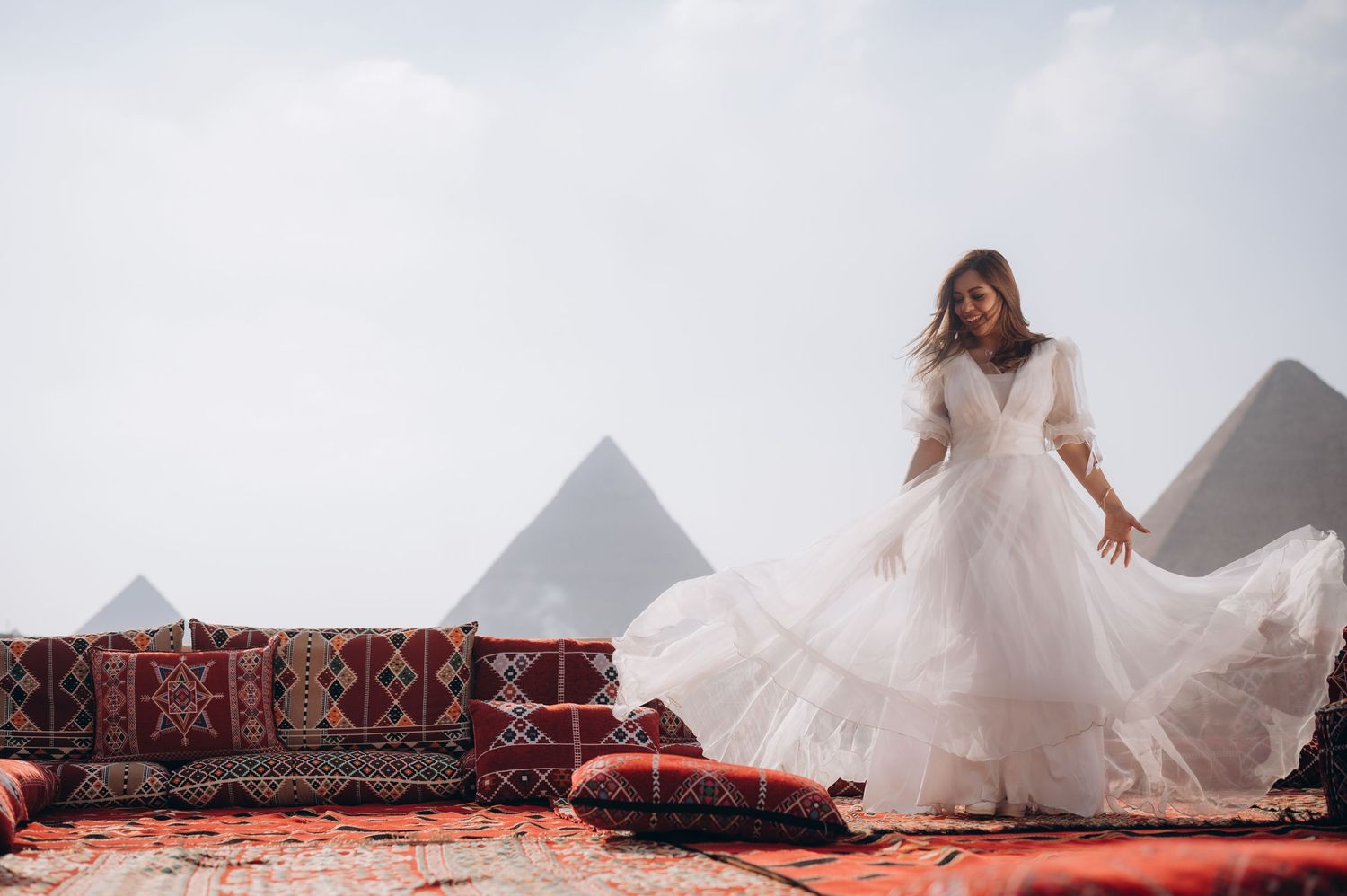 A white wedding dress flows in the wind with the Egyptian pyramids creating a stunning backdrop.