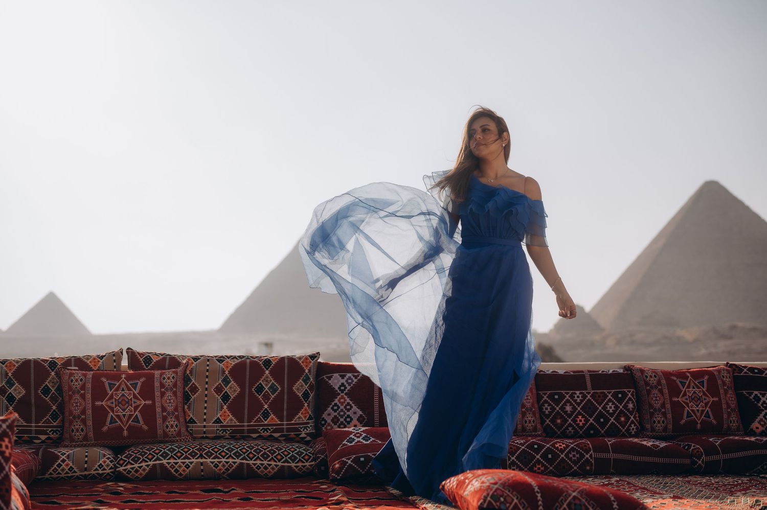 A flowing blue dress catches the wind against the majestic backdrop of the Egyptian pyramids.