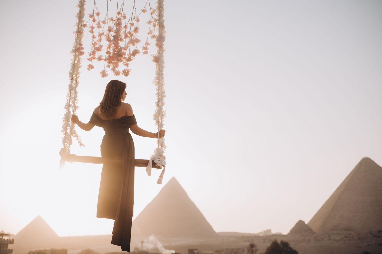 A silhouette poses on a decorated swing with the pyramids of Giza visible in the background.