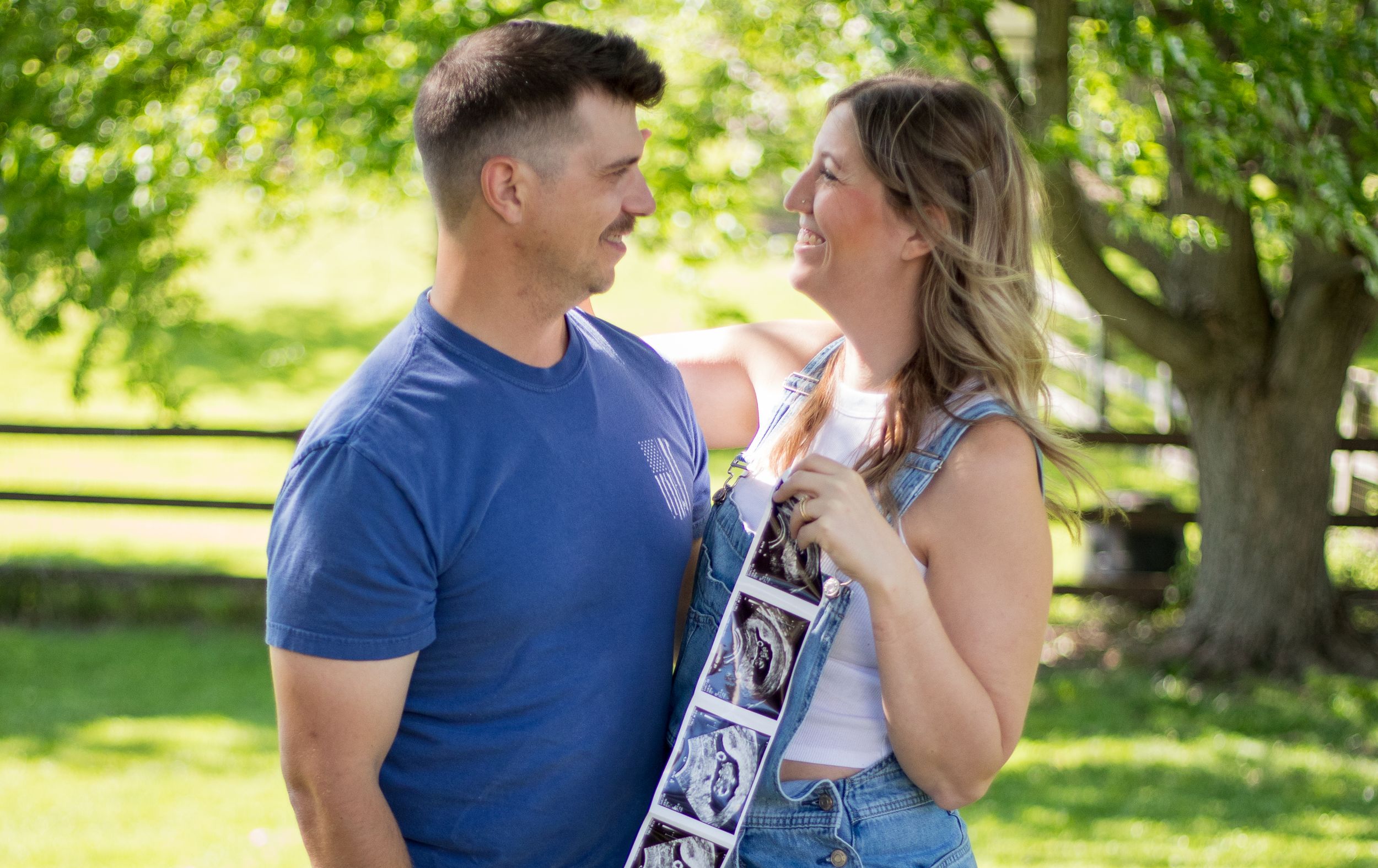 Couple shares a joyful moment holding ultrasound photos in a sunny green yard