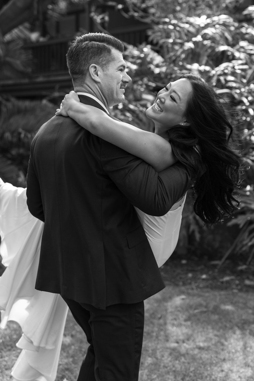 A joyful black and white photograph of a couple embracing during their wedding, with the bride's hair flowing in the breeze.