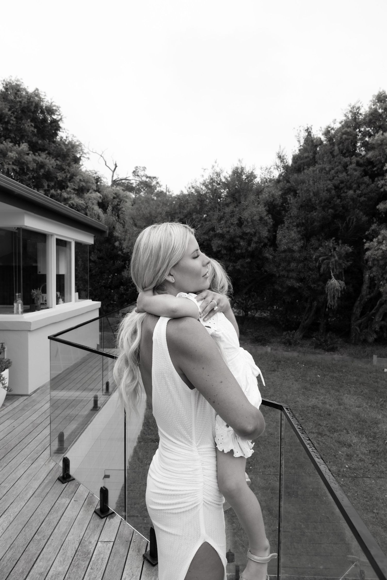 Woman in white dress takes a celebratory drink on an outdoor deck.