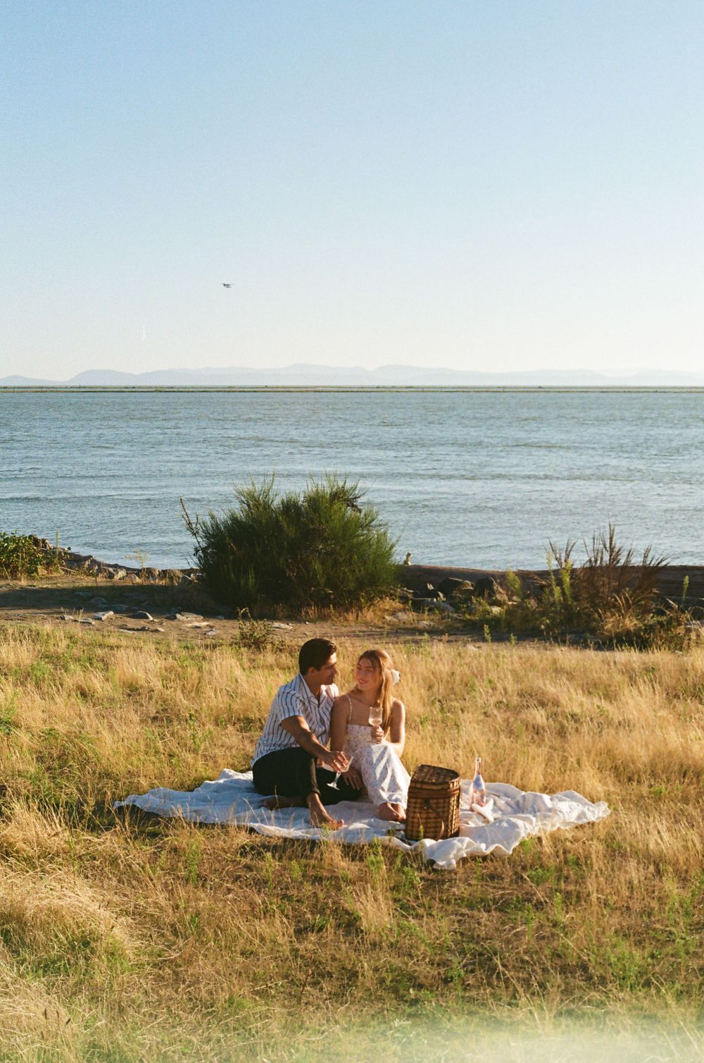 Seaside picnic scene with blanket spread out on grassy coastal bluff.