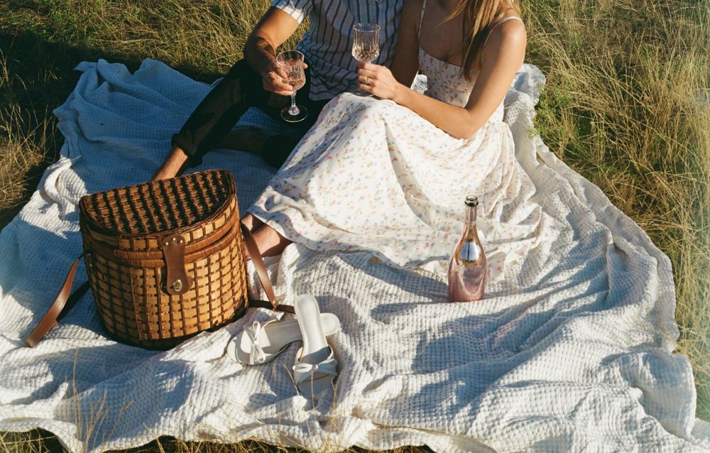 Picnic scene with wicker basket and couple on white blanket.