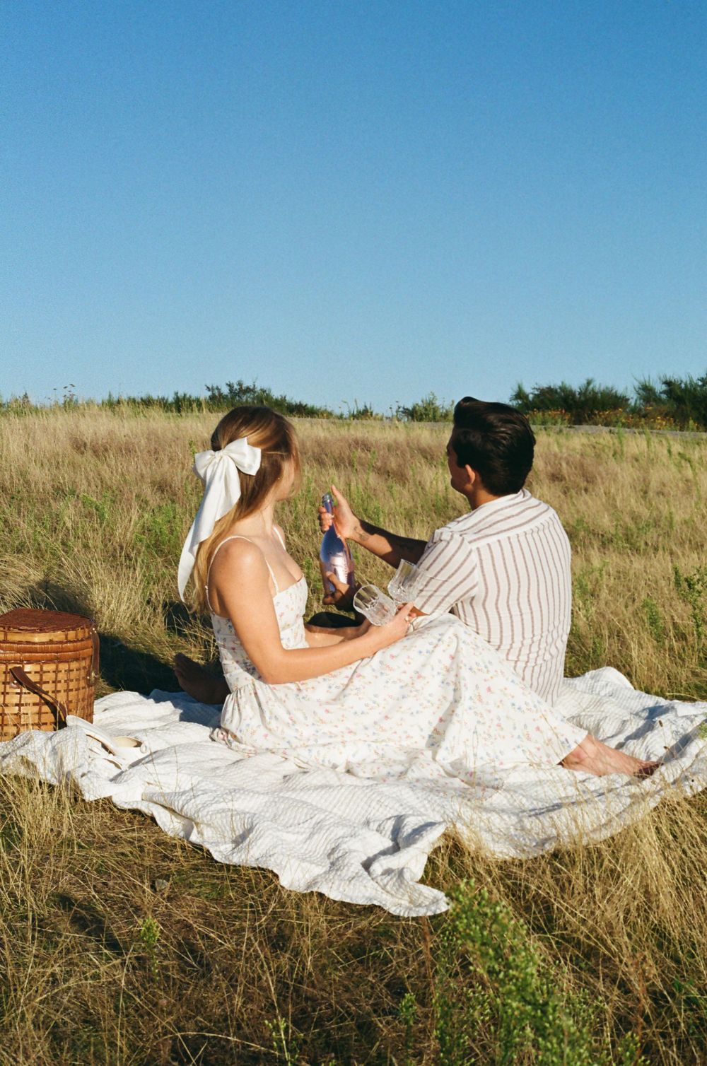 Summer picnic on white blanket with wicker basket in golden field.