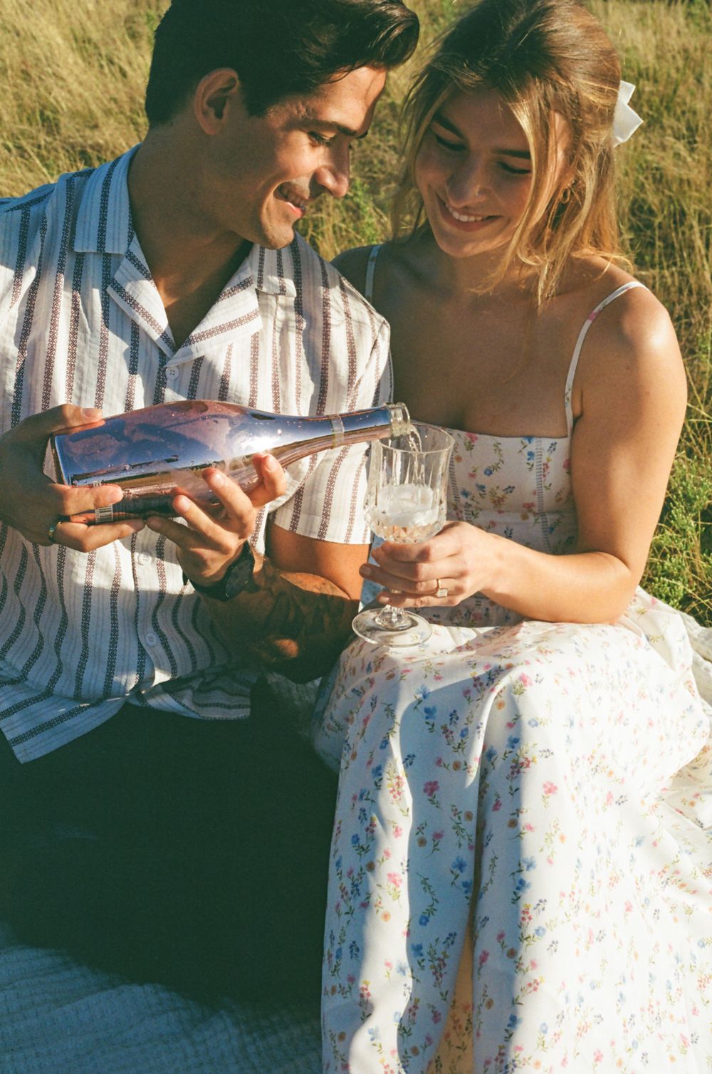 Intimate picnic moment with champagne pouring in sunny field.