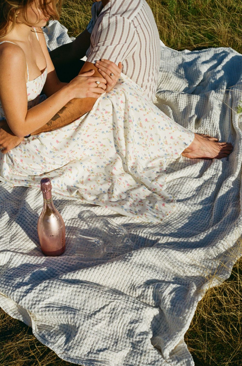 Romantic picnic setting with floral dress and white blanket on grass.