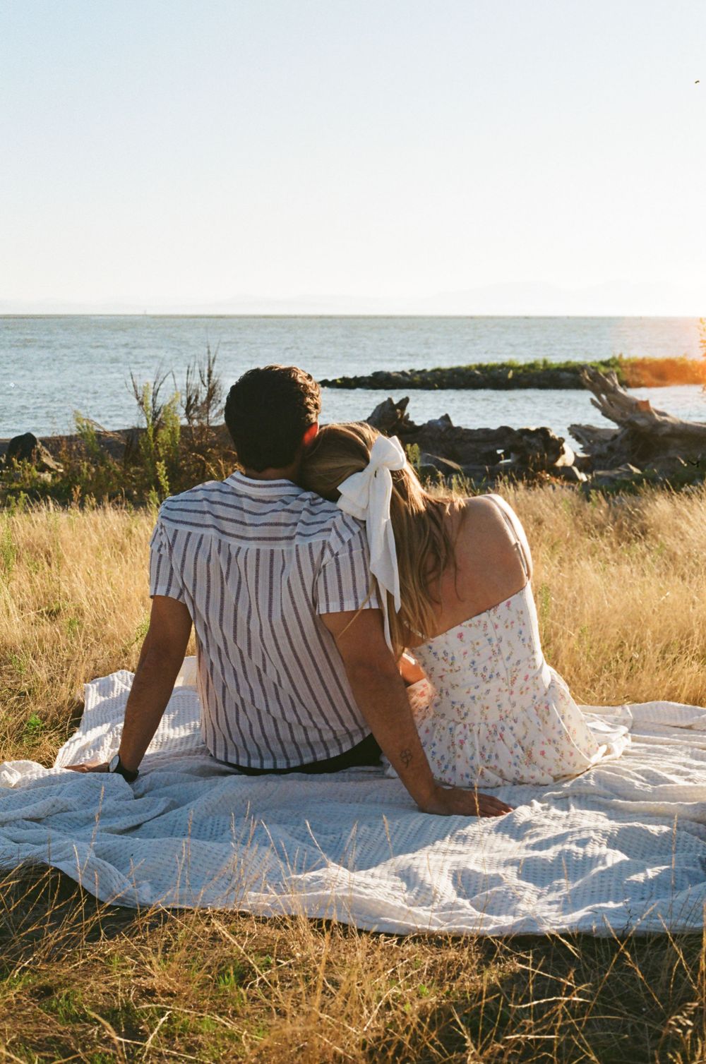 Two people laying on a blanket in warm evening light with coastal views.