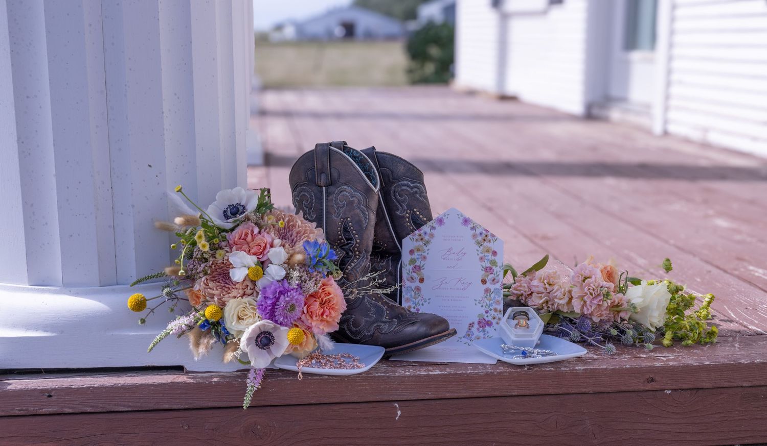 Wedding detail flat lay featuring cowboy boots, floral arrangement, invitations, and jewelry in Dawson and Bismarck North Dakota wedding