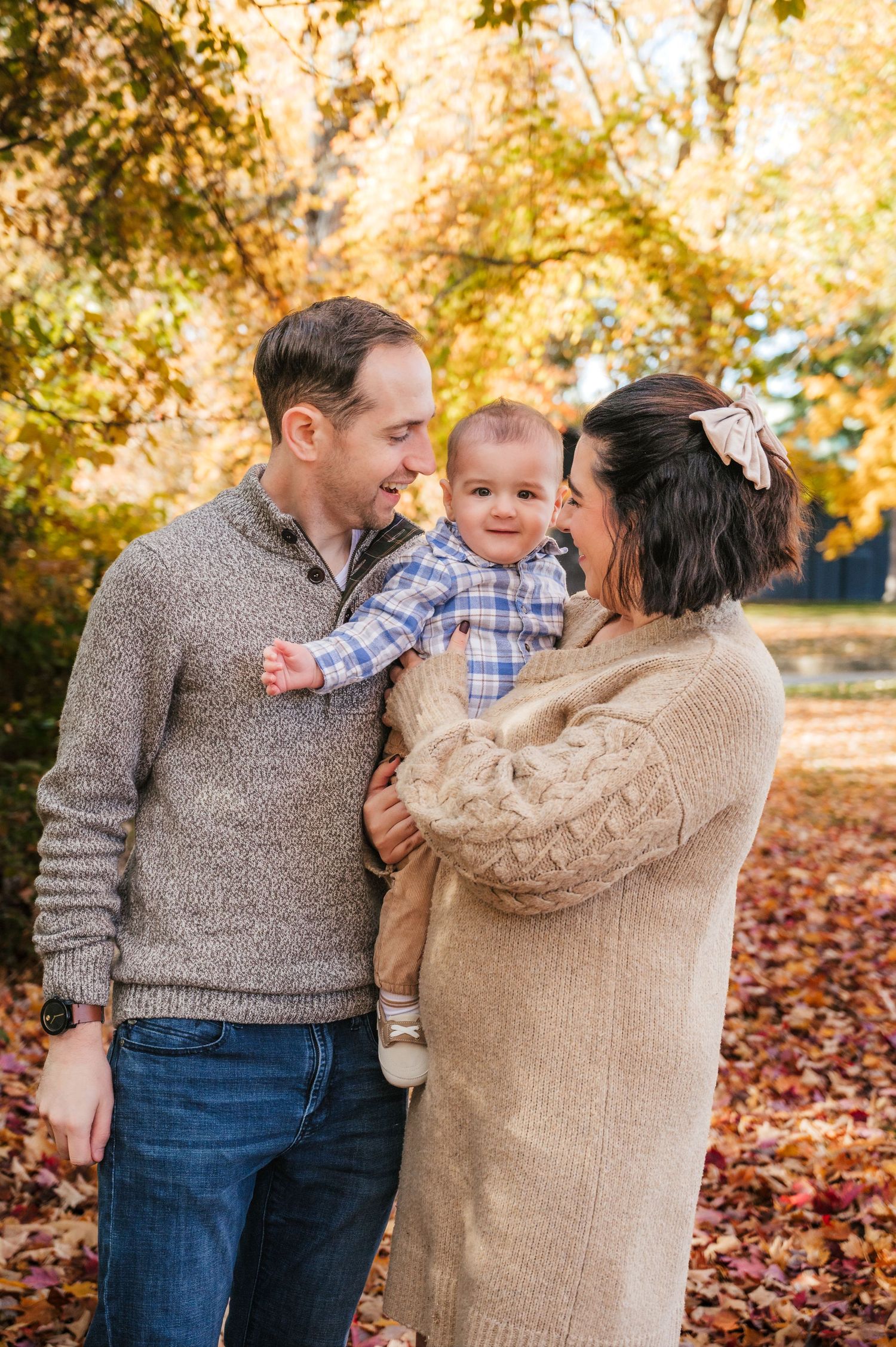 Family in cozy sweaters share joyful moment together on autumn day with fallen leaves in background.