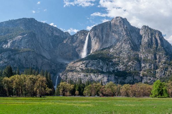 Stunning Yosemite Falls cascading down granite cliffs above a lush green valley meadow.