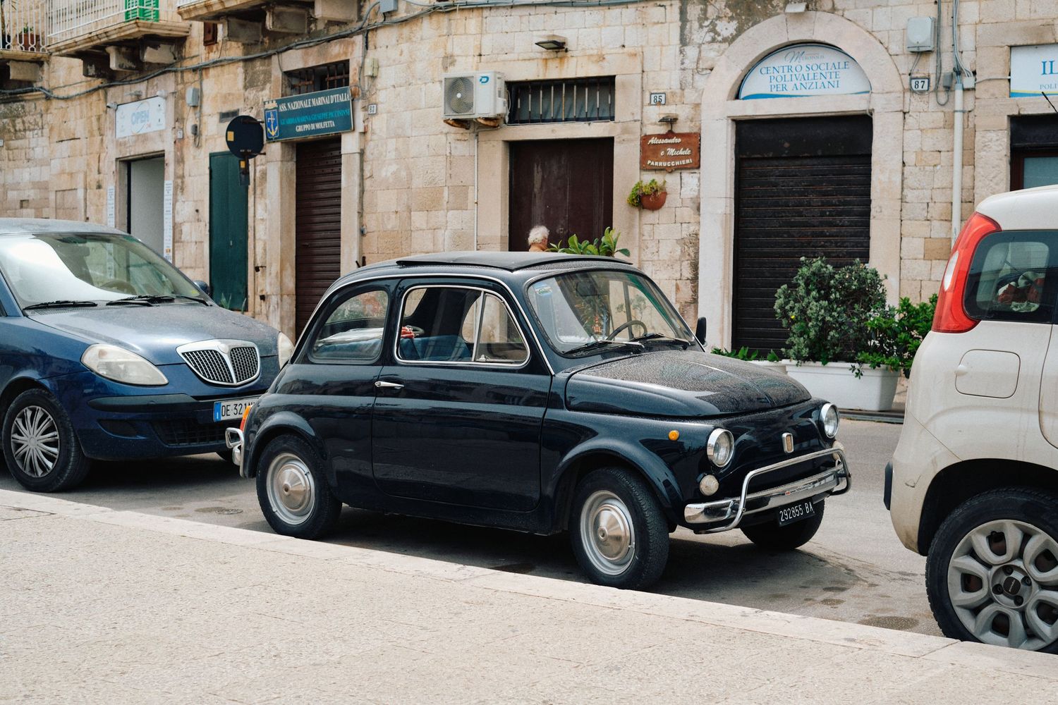A classic Fiat 500 parked between modern cars on an Italian street.