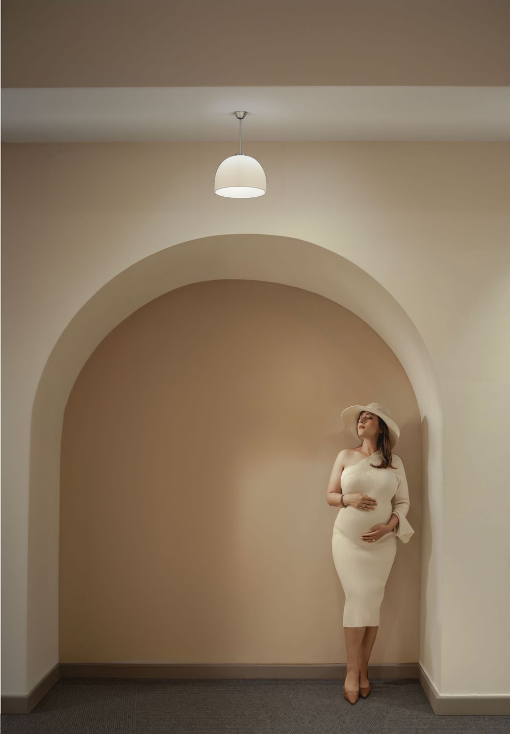 Minimalist maternity photo under an arched doorway with pendant light.