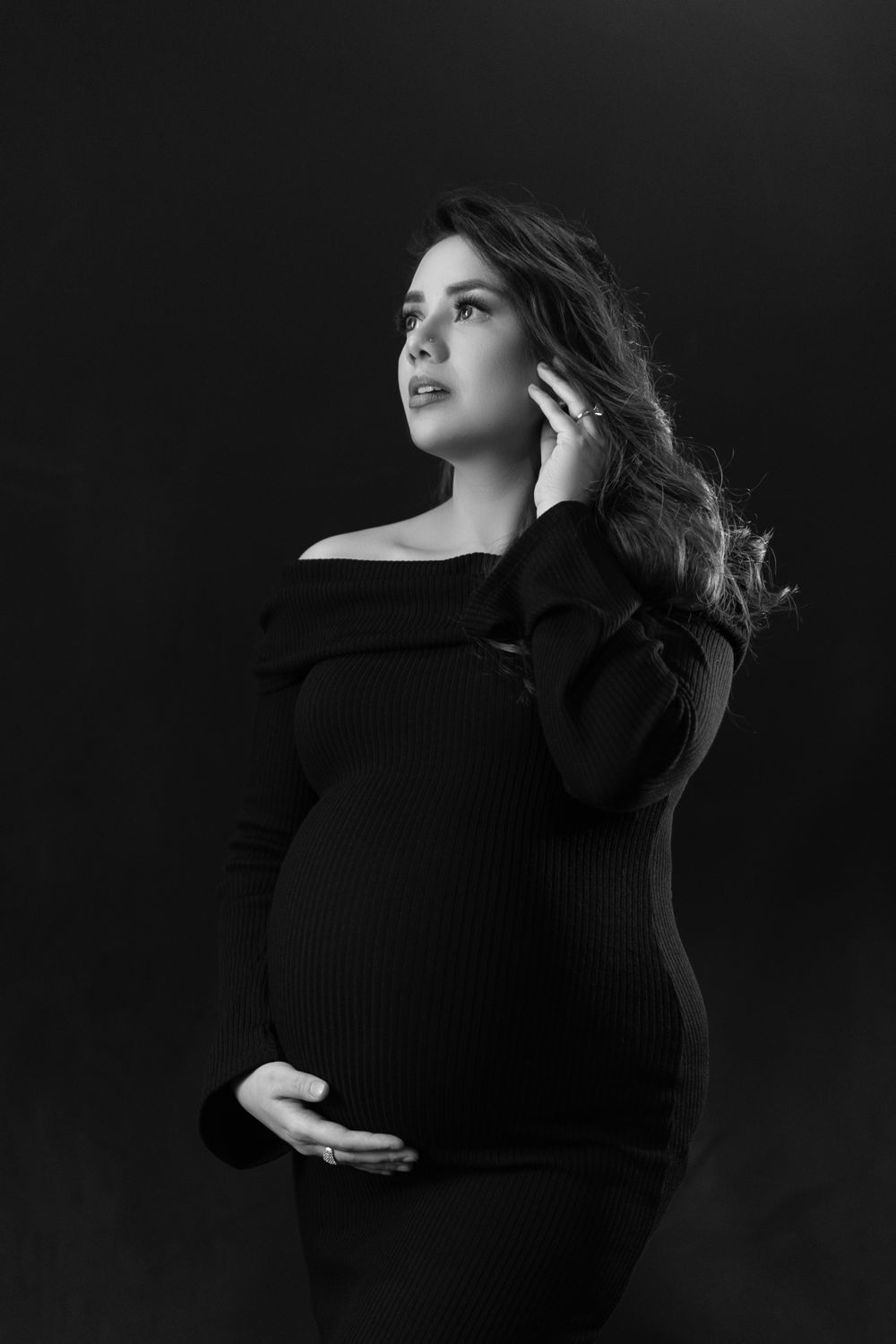 An artistic black and white maternity portrait showing an expectant mother in an off-shoulder dress.