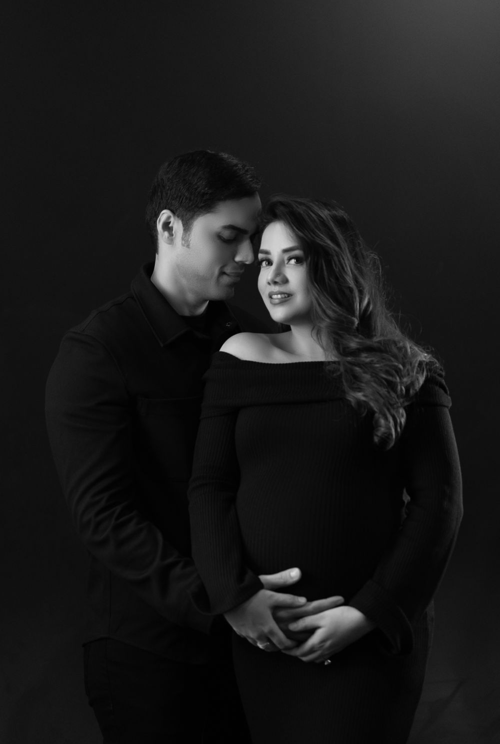 Intimate black and white portrait of an expecting couple embracing in dark formal wear.