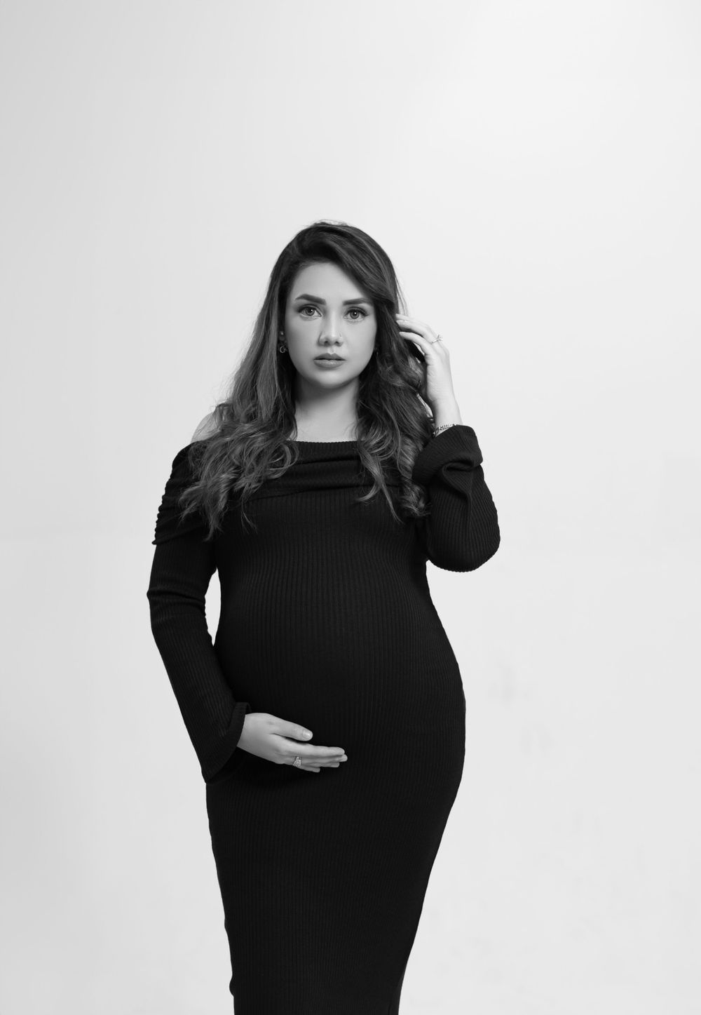 Monochrome maternity portrait against white background in fitted black dress.
