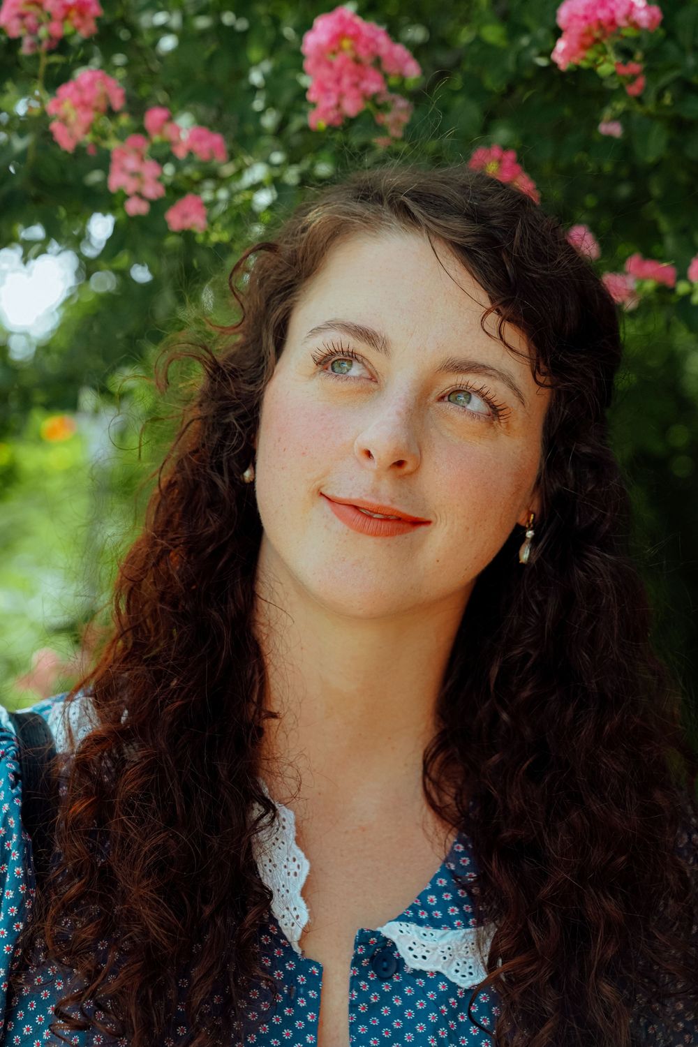 Portrait photos outdoors with pink flowers in background, wearing blue dress with white collar.
