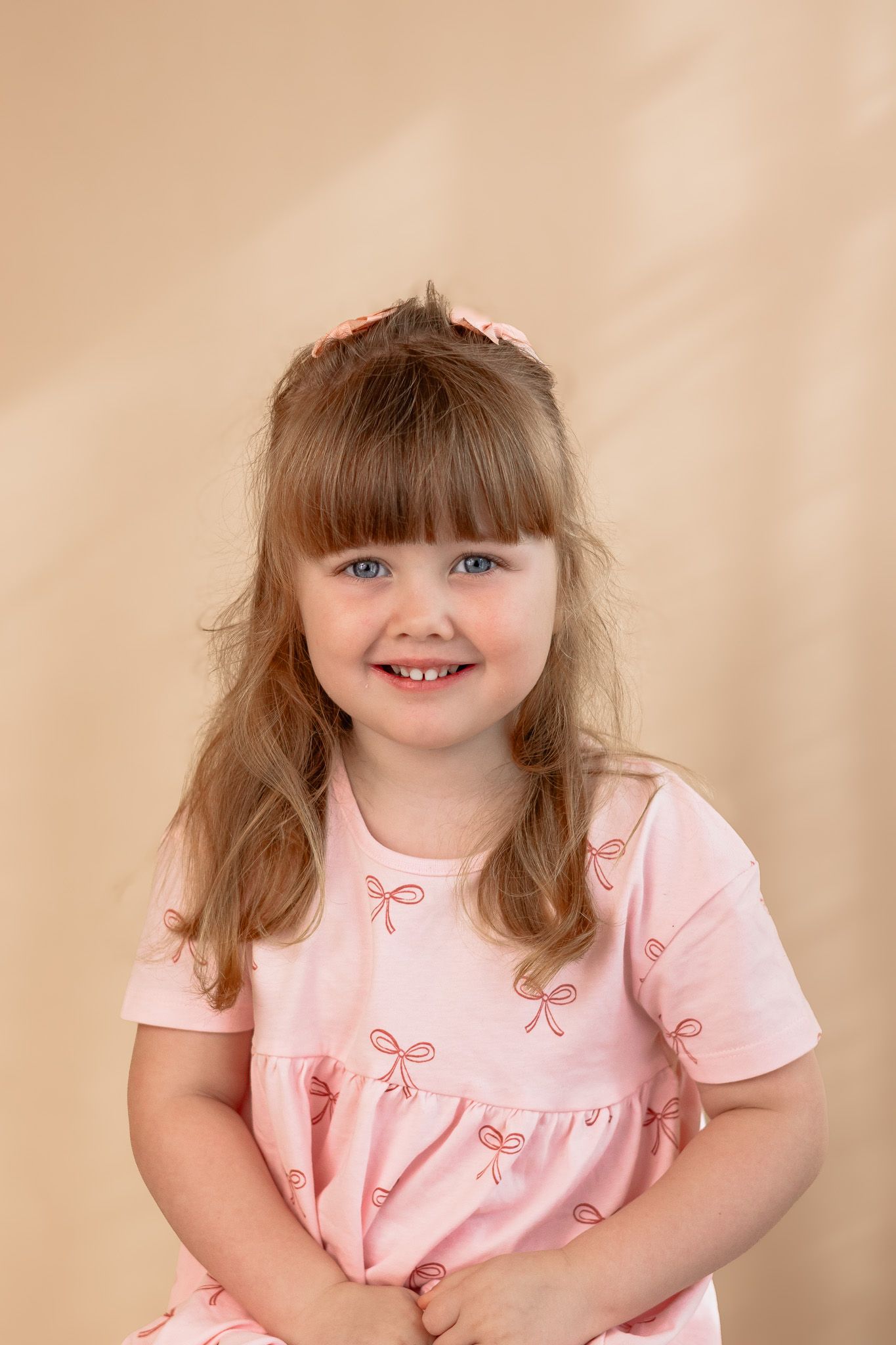 Studio portrait against a peachy backdrop wearing a pink bow-patterned dress.
