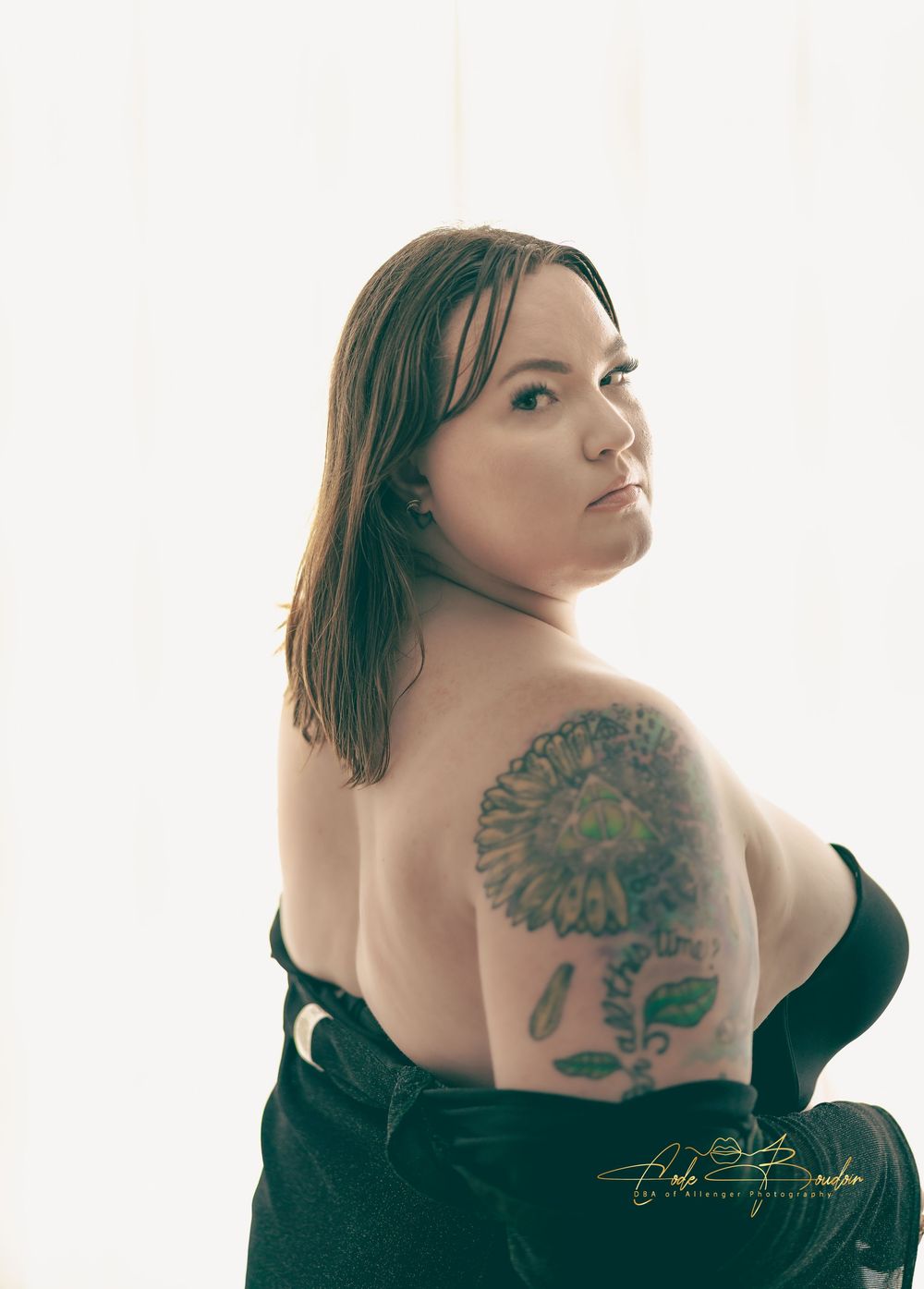 Woman posing for a boudoir sheet wearing black lingerie standing in front of a lit window.