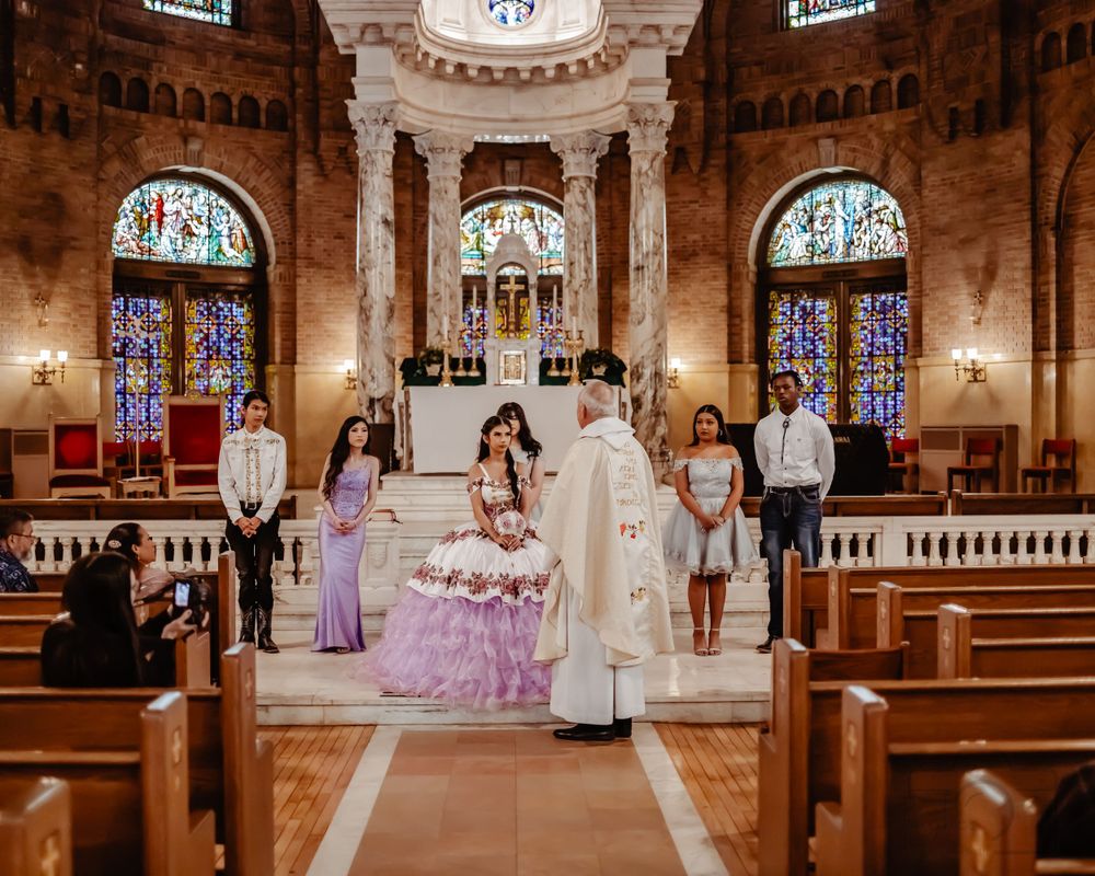 Traditional quinceañera ceremony in church featuring lavender gown and ornate stained glass windows.Quinceanera