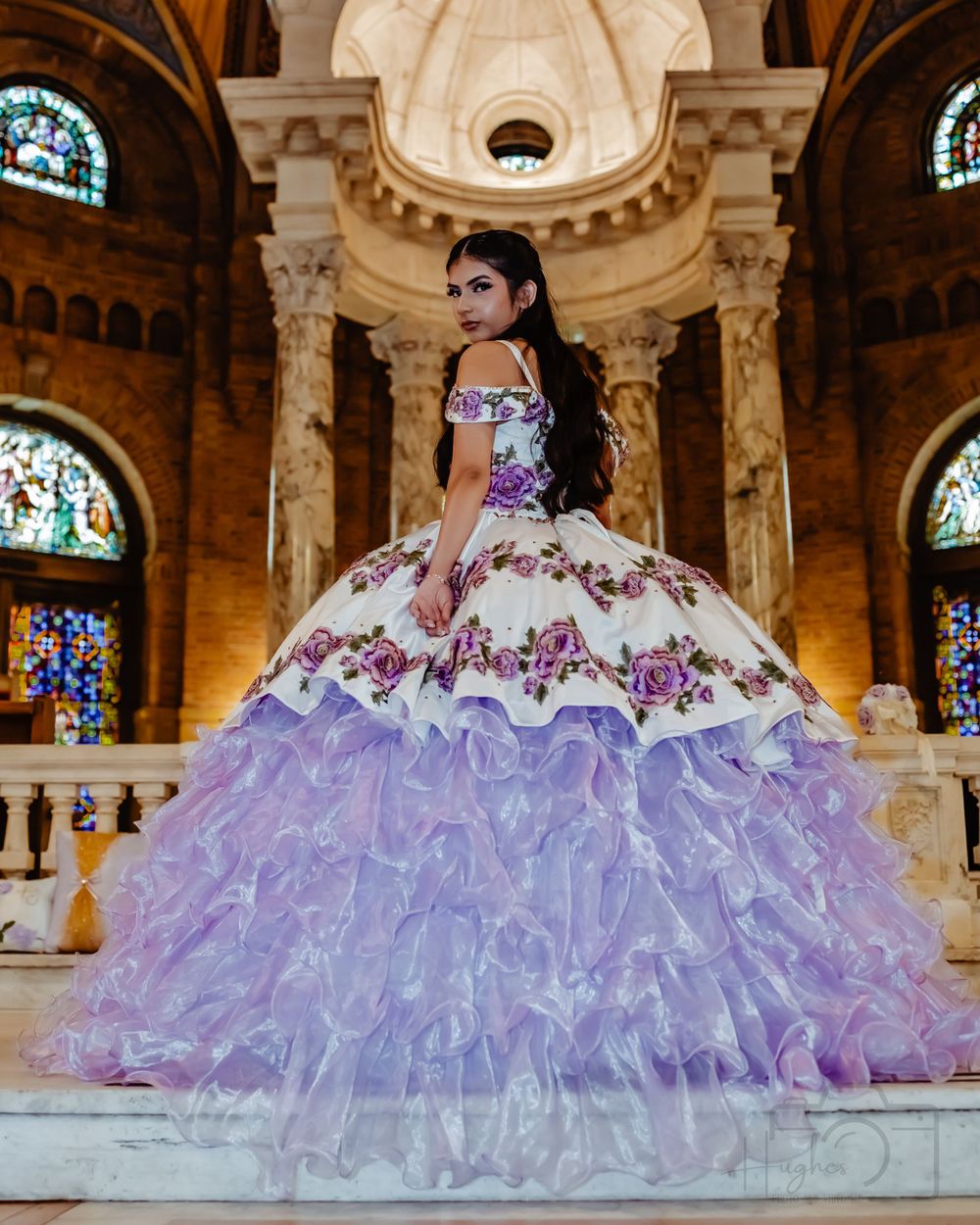 Stunning quinceañera dress with purple floral details and ruffled skirt in grand church setting.
