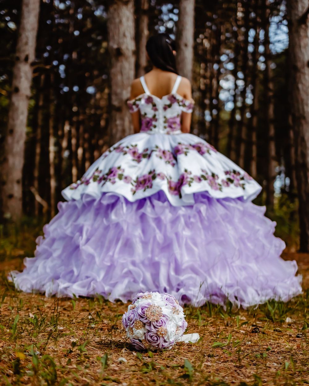 Dramatic ballgown with purple ruffles and floral details captured from behind in a forest with bouquet.