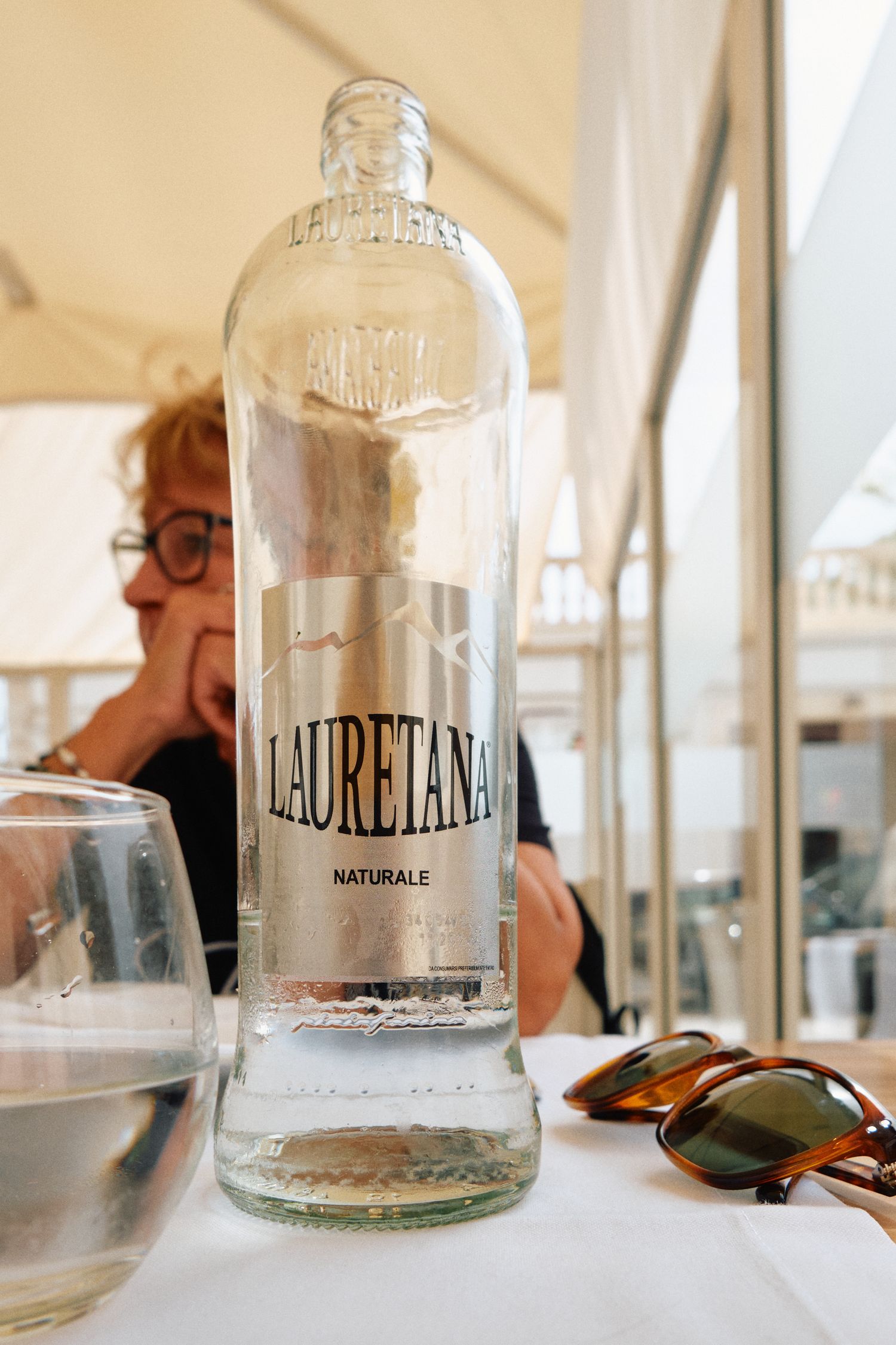 A clear glass bottle of Lauretana natural water on a restaurant table.