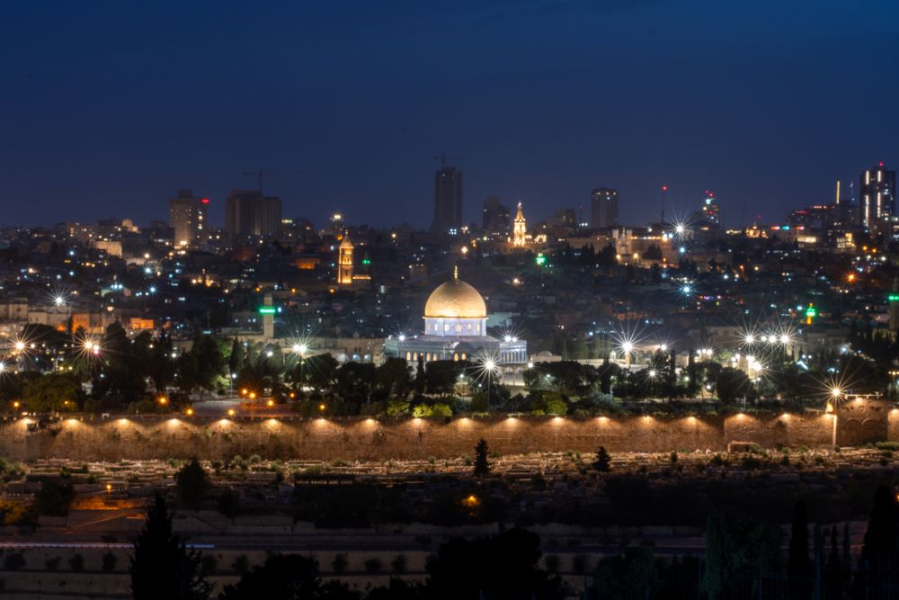 Night view of Jerusalem with illuminated Dome of the Rock and city skyline.