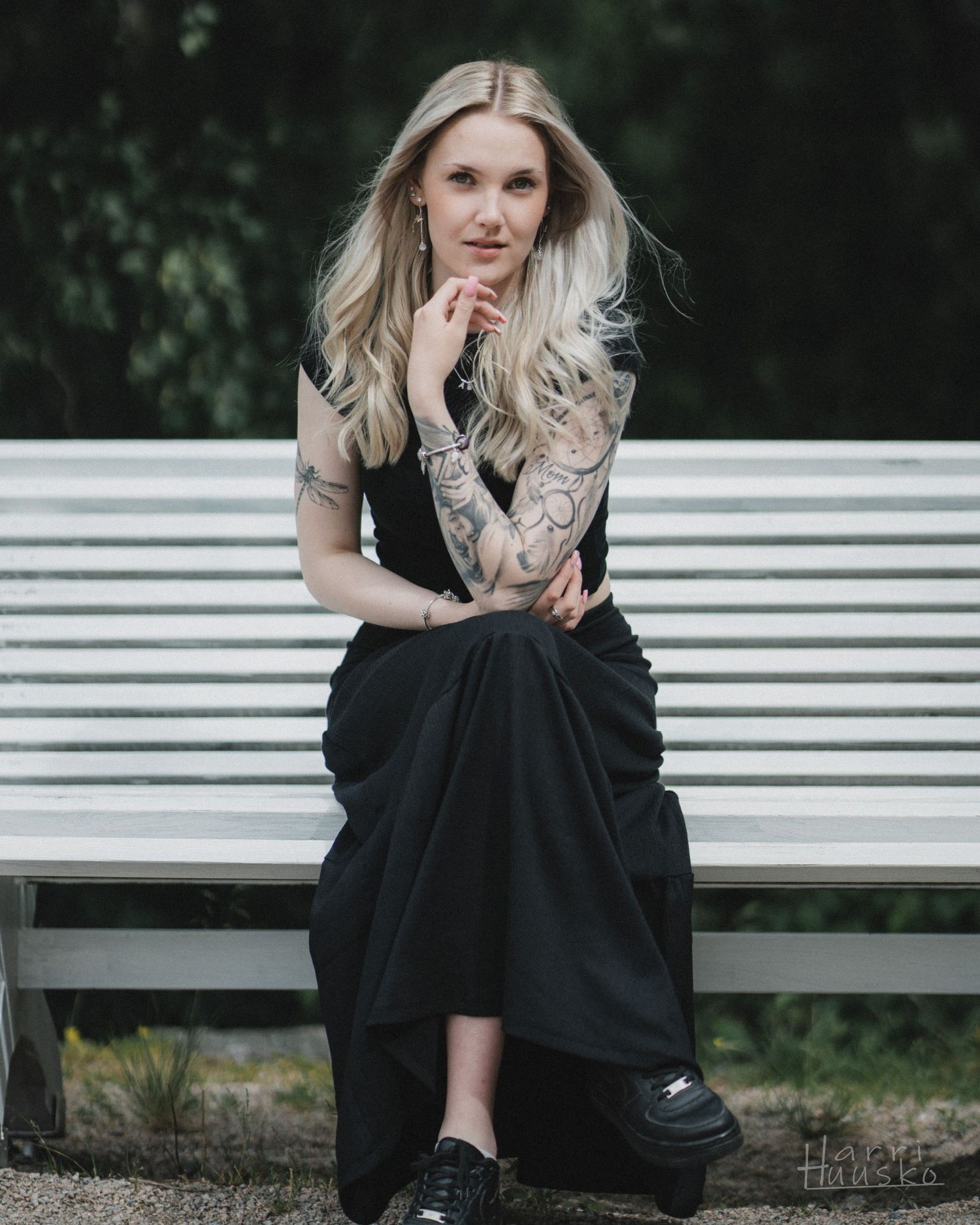 A person in a black dress sits thoughtfully on a white bench outdoors.