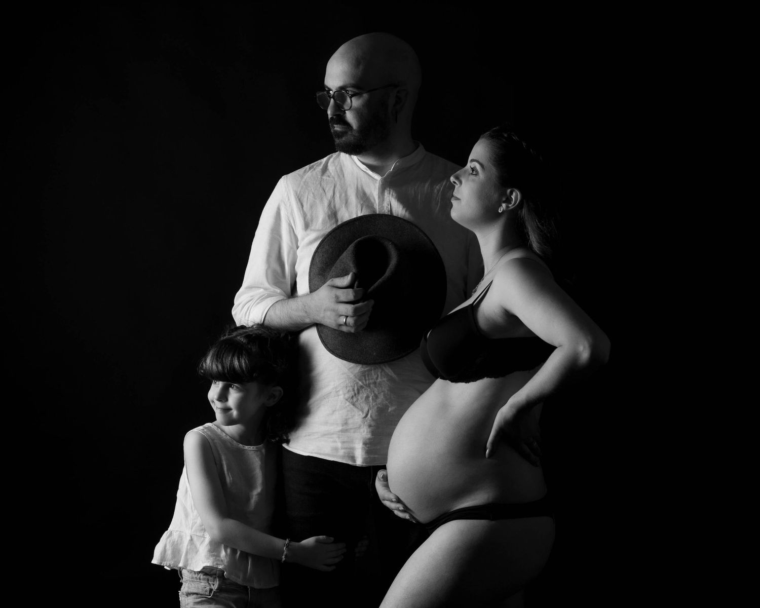 Dramatic black and white family maternity portrait with child against dark backdrop.