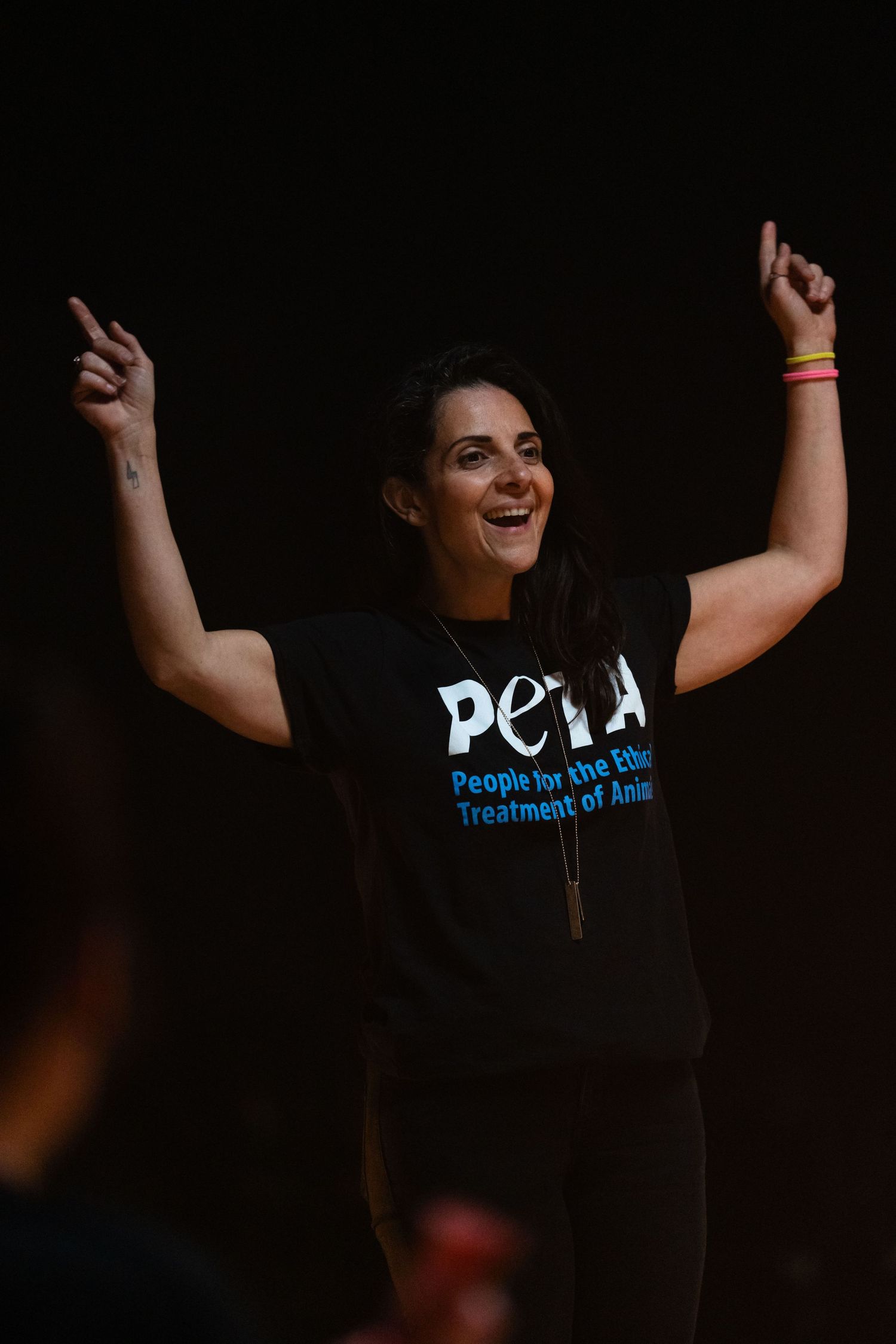 Performer in PETA t-shirt raises arms triumphantly during stage performance.