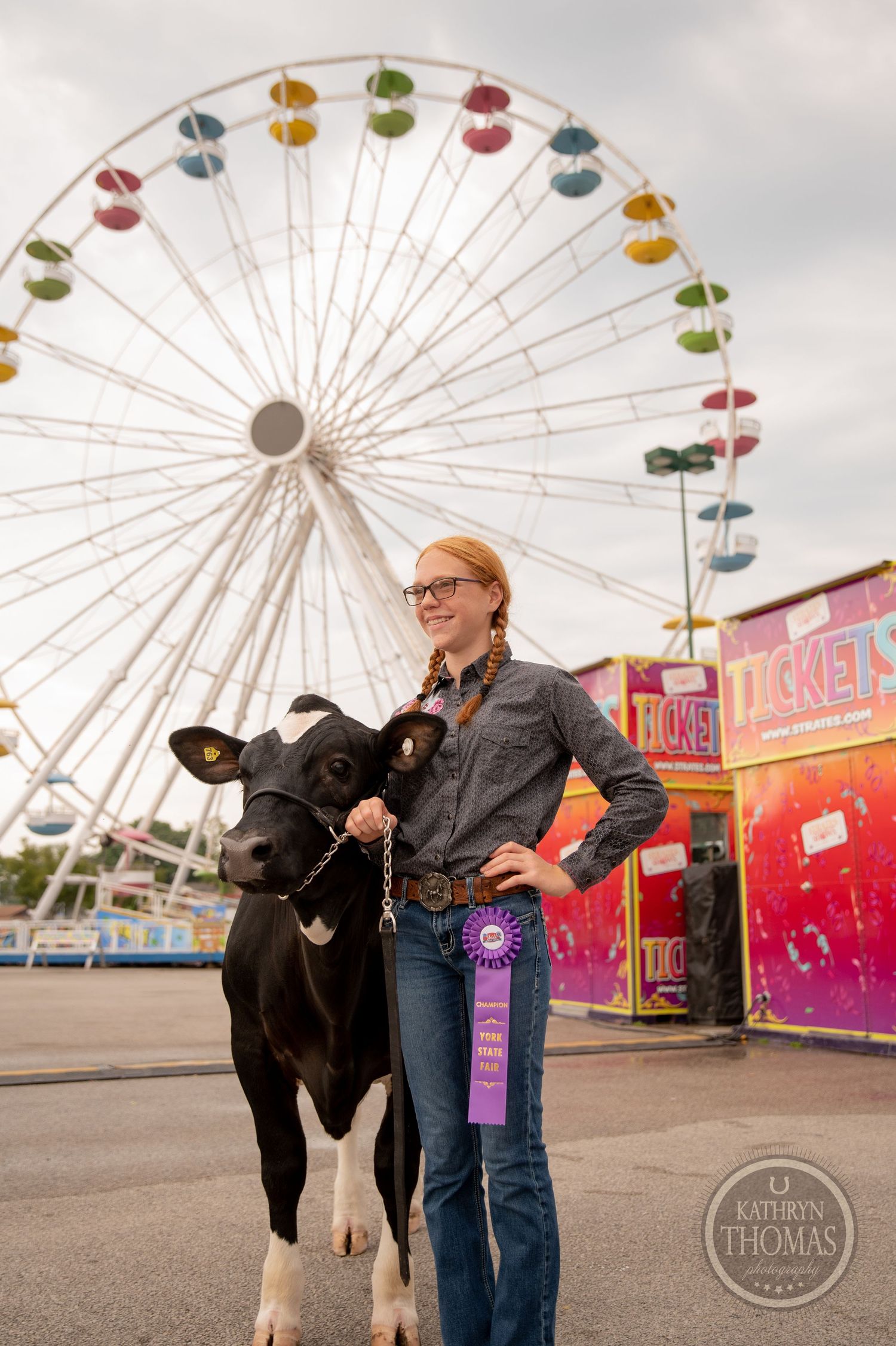 Award-winning dairy cow poses with handler in front of colorful ferris wheel at county fair.