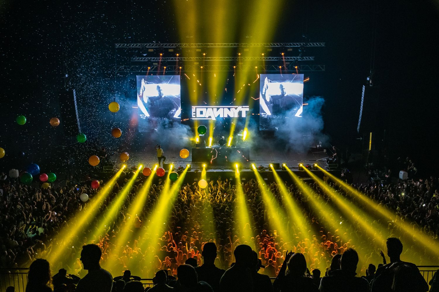 Concert stage illuminated with bright yellow spotlights and smoke effects during nighttime performance.