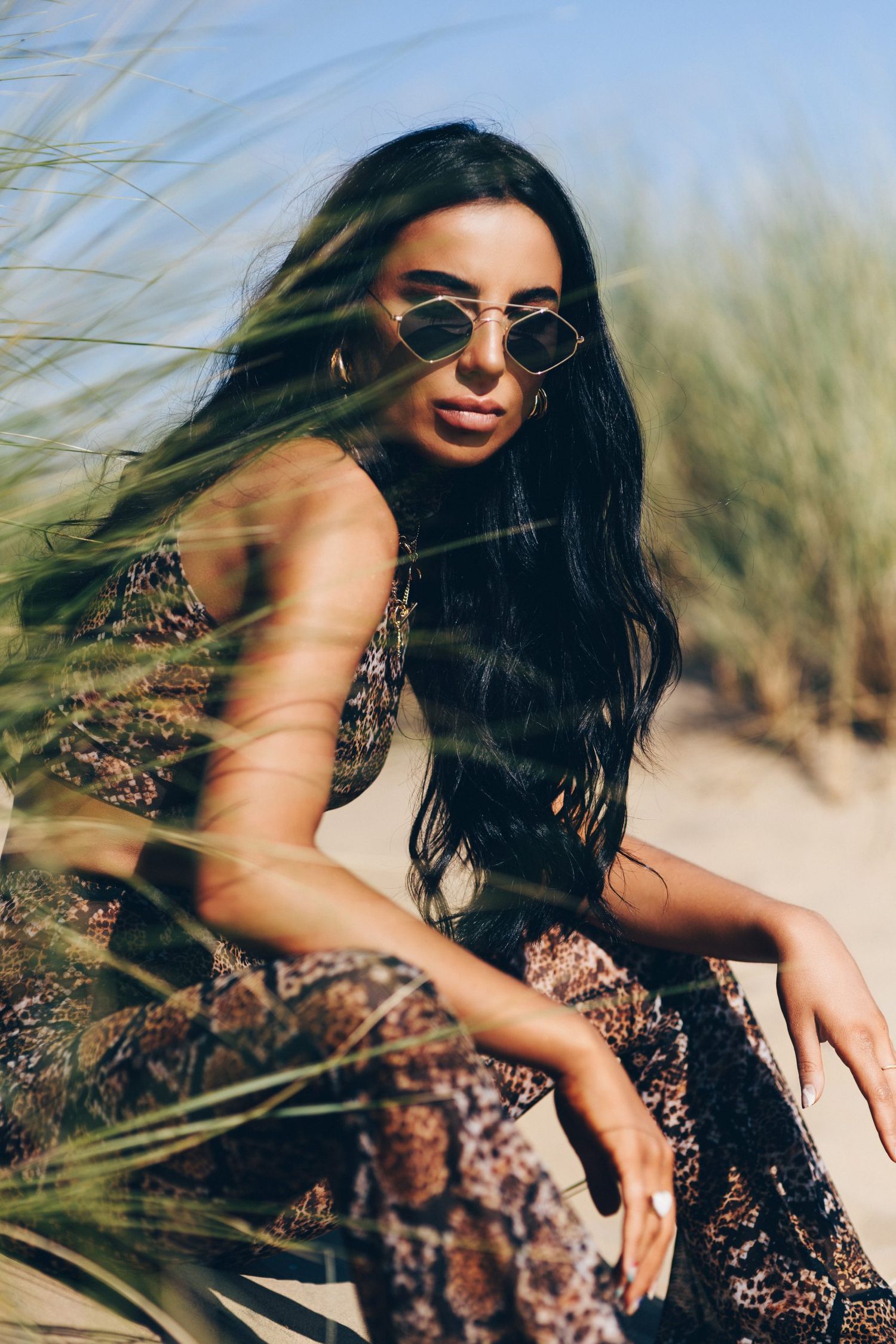 Fashion model in floral dress poses dramatically against beach grass in warm sunlit photo series.