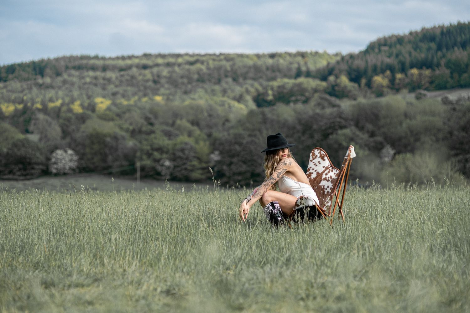 Person lying in tall grass field with mountain landscape in background.