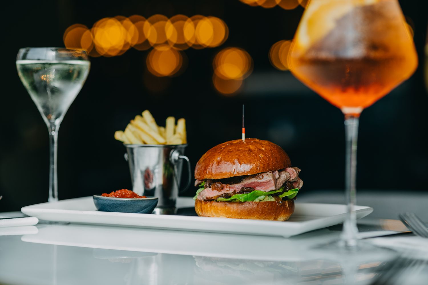 Gourmet burger and french fries served with martini and cocktail in elegant setting.