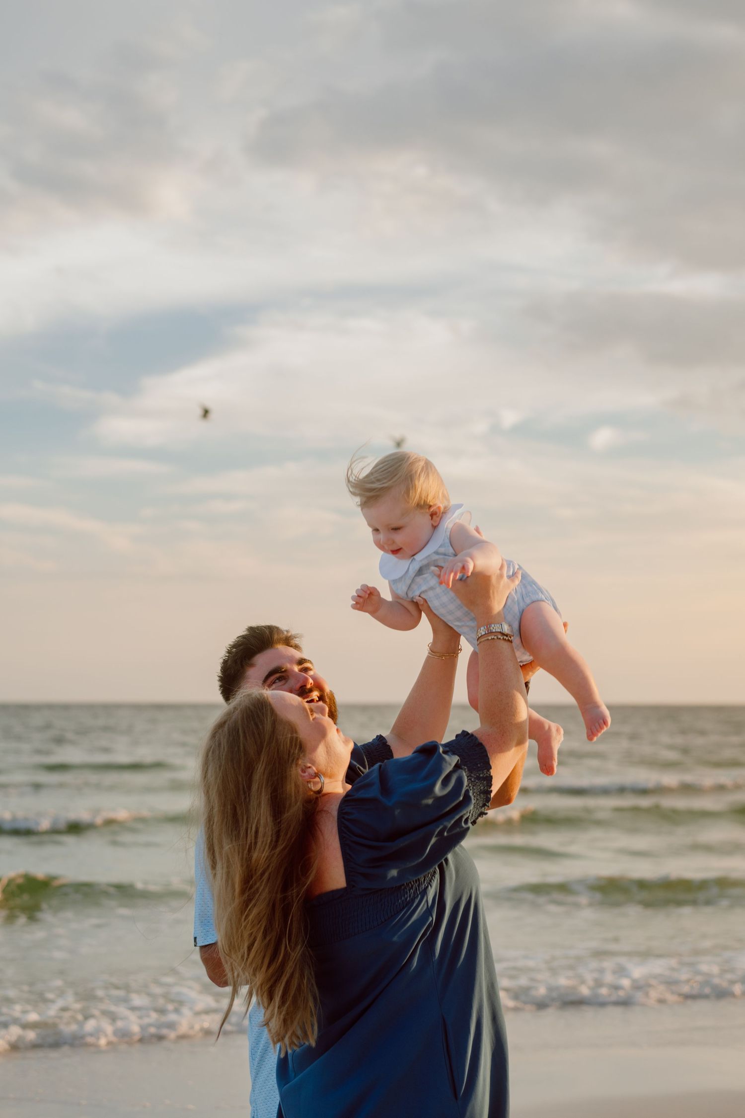 Playful moment lifting baby against the backdrop of an ocean sunset.