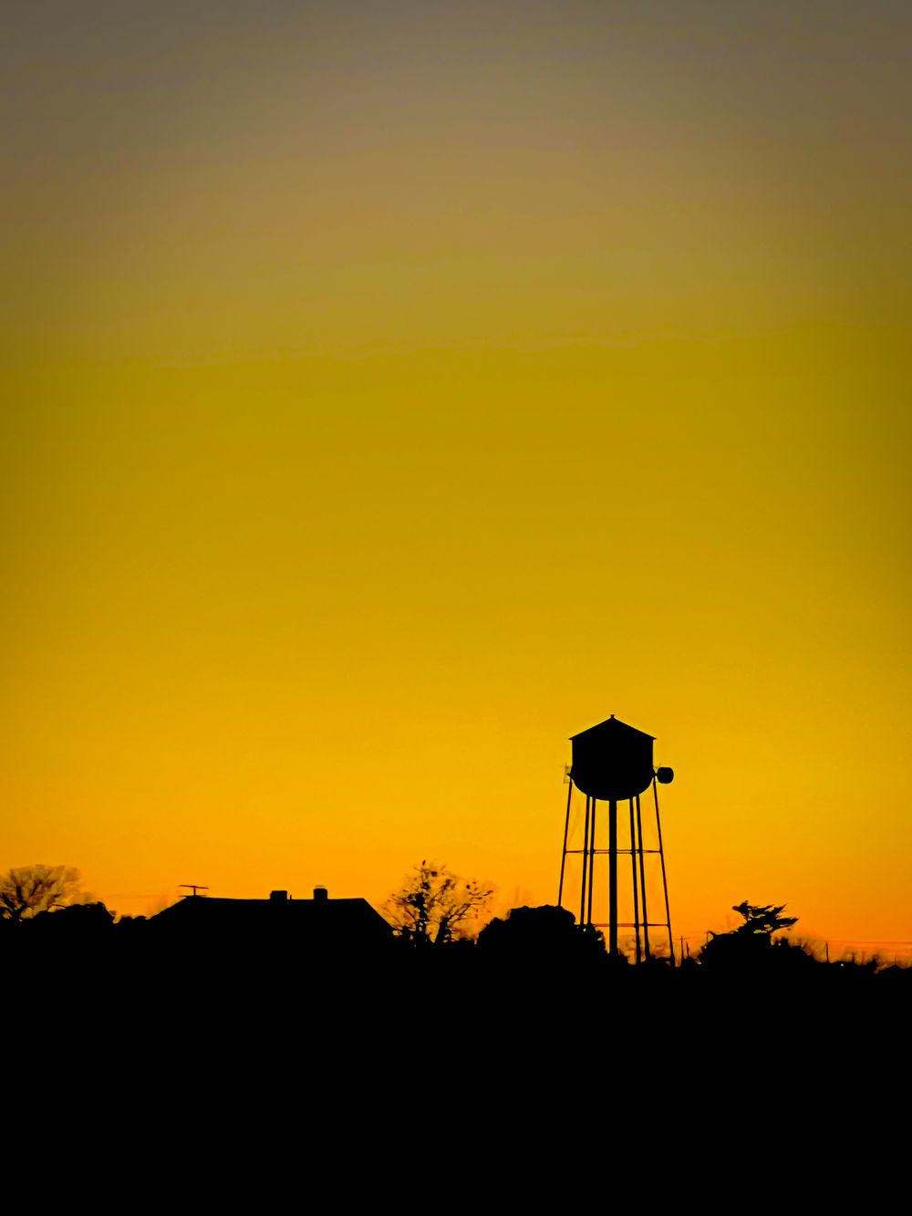 Water tower silhouette against golden sunset sky in rural setting.