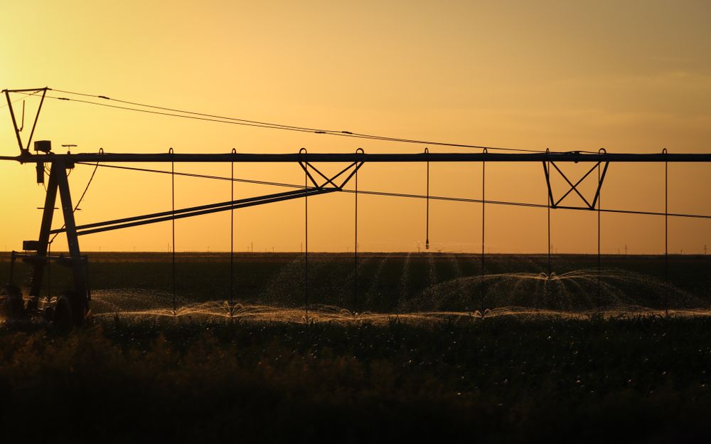 Center pivot irrigation system silhouetted against golden sunset sky.