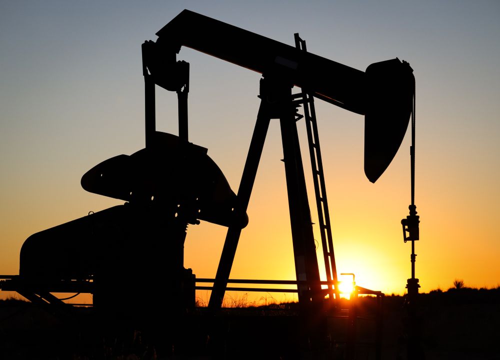 Oil pump jack machinery silhouette backlit by bright setting sun.