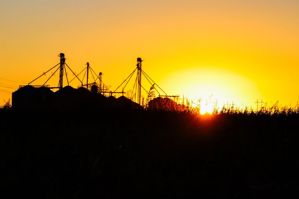 Silhouette of grain silos against a vibrant orange sunset sky.