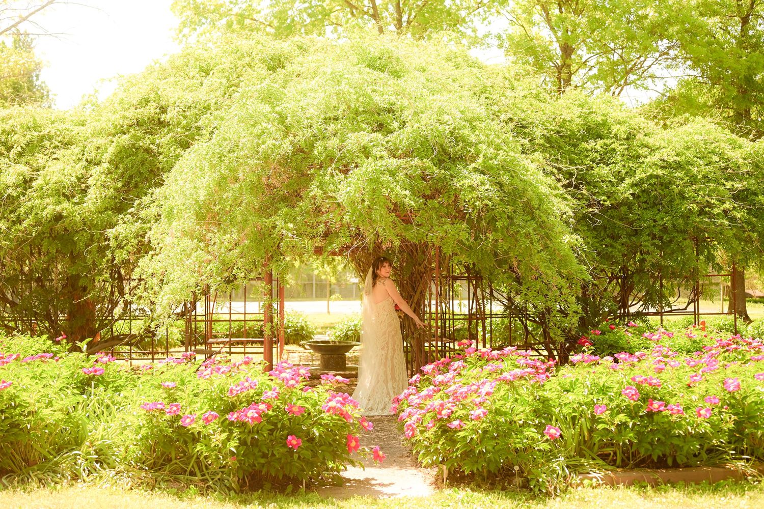Bride and groom share a romantic moment in a lush garden with blooming pink rhododendrons.