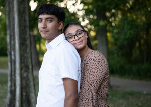 Young couple in white shirt and floral dress pose back-to-back outdoors.