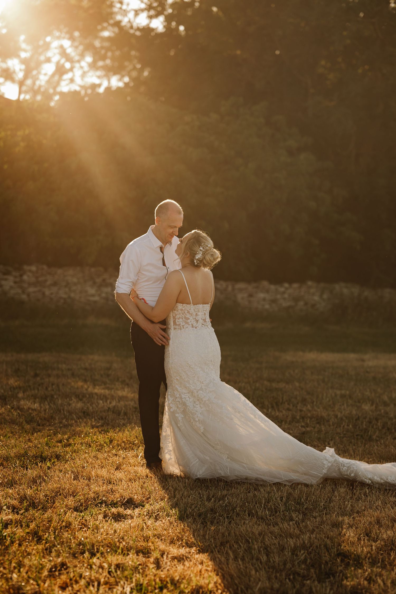 Couple shares romantic embrace in golden sunset light in open field at outdoor wedding.